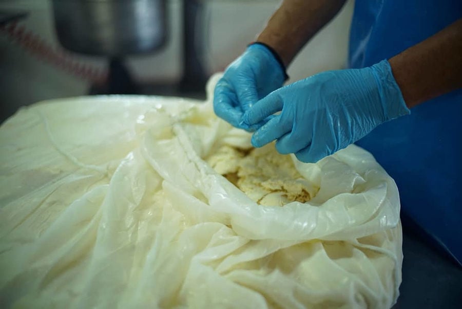 man with gloves making cheese from plastic bags at 'Mykonos Farmers' plant